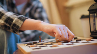 Close up of person hand moving game pieces on checkers board. person interacts with wooden checkerboard placing or shifting dark and light