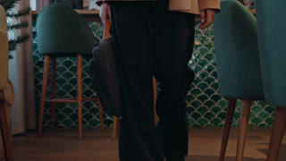 Caucasian entrepreneur exiting cafe with briefcase, green chairs, bistro stools, wooden floor, brisk stride, business casual attire, leather