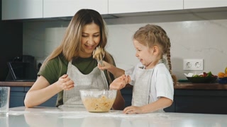 Slow motion: adorable child plays with dough, cooking with parent in modern kitchen at home