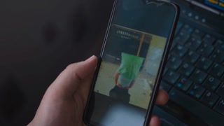 Man watches video of girlfriend kidnapping victim with bag on head via mobile phone and blows smoke near laptop in semi-dark room closeup slow motion