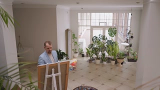 Middle aged artist painting female model on canvas in his art studio