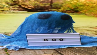 Halloween holiday concept. Handmade blue ghost made from bandages and glue with Lightbox BOO text in autumn forest background. Children's