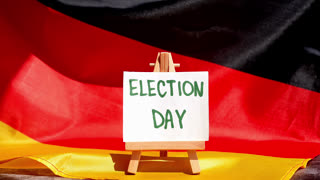 Paper note with words ELECTION DAY on National symbol of Germany. German wave silky flag background. Concept of election political