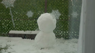 A snowman stands in the courtyard of an apartment building. It is formed from two large snow boulders. Snow covers the ground, creating a winter scene.