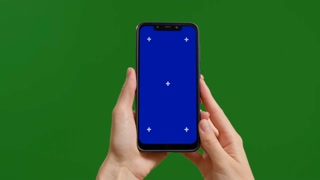 Female holds blue chroma key device vertically with fingers on green screen background. Phone user hands watch blue chroma key screen.