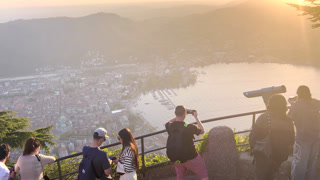 Como Lake, April 10, 2026: People enjoying panoramic viewpoint in Brunate overlooking Lake Como at sunset, tourists admiring city, mountains and scenic Italian landscape from terrace