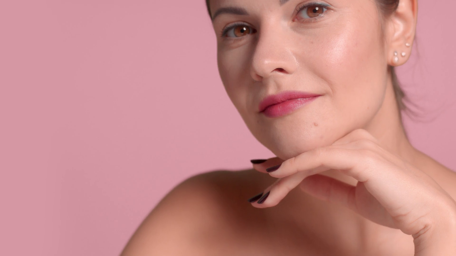 30s brunette woman wears a decollete top with ideal skin in studio on pink background pan camera movement picture