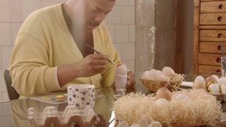 man in sunny room painting easter eggs