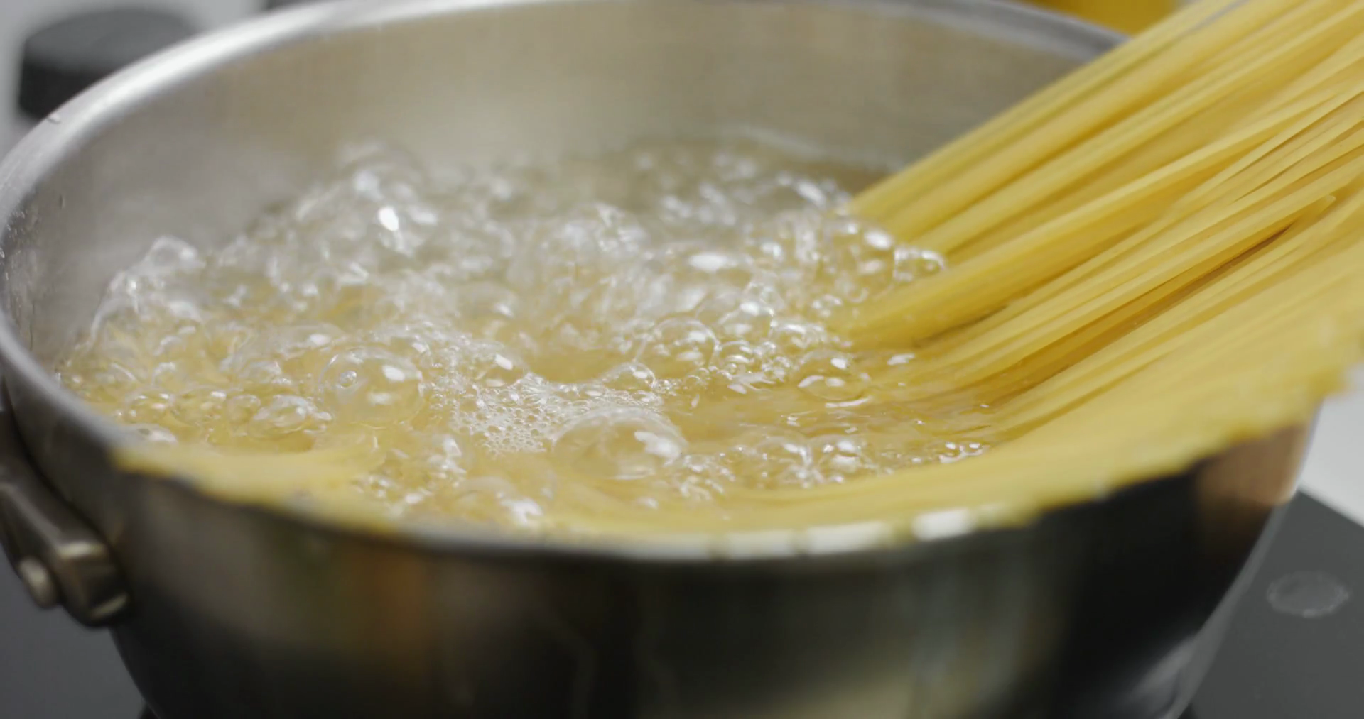 Spaghetti boiling on high heat in a large stainless steel pan, close up