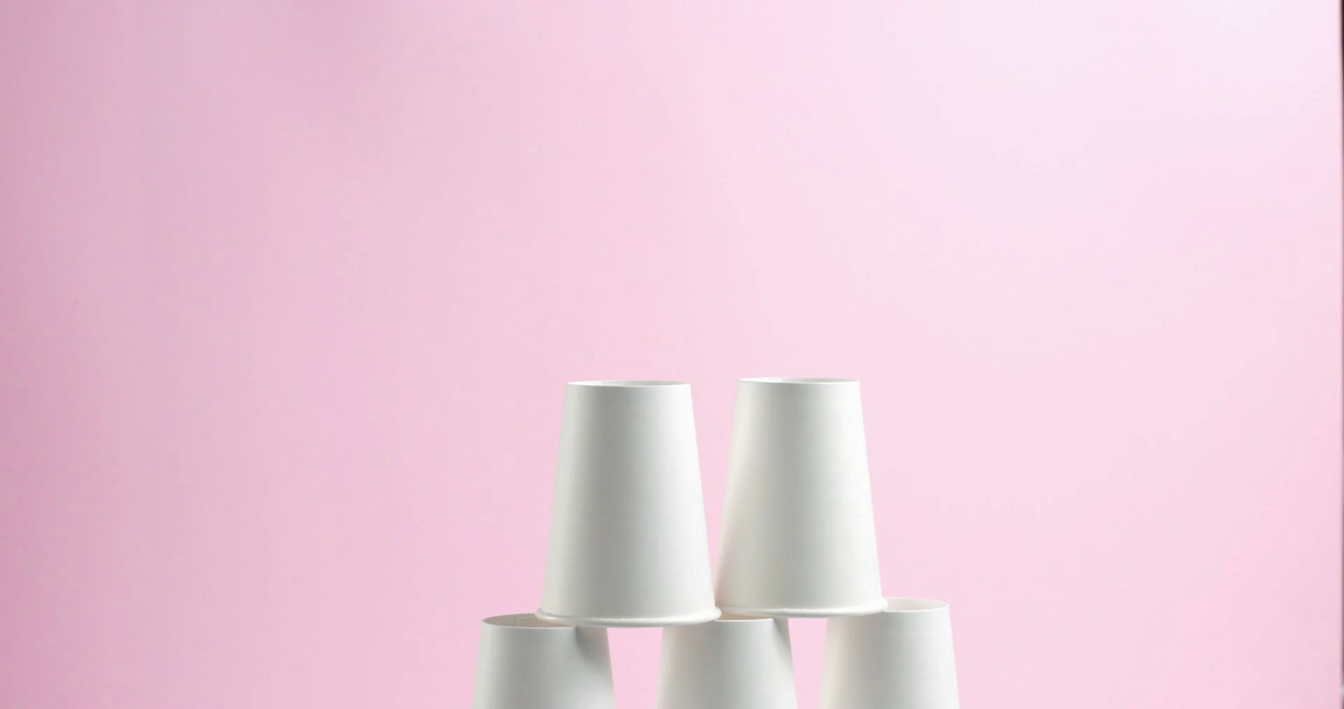 Young woman builds and breaks tower pyramid of white paper cups turned ...