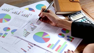 Analyzing financial reports and charts with a pen on a wooden office desk top