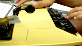 Hands typing on a vintage yellow typewriter with black keys in a bright office space