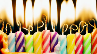 Close-up row of colorful birthday candles burning in timelapse on black. Rainbow background, multicolored melting wax burning candle shot in time-lapse. Happy Birthday, family holidays celebration