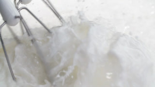 Close-up slow motion electric mixer whips fresh milk cream, whisking milk in bowl