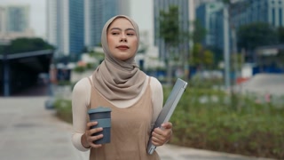 Portrait of Muslim woman in hijab walks carries laptop and coffee cup in city