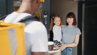 A happy food delivery man in a thermal backpack delivers an order to a beautiful client with a child from a restaurant. The courier delivers