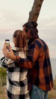 A couple shares a tender moment as they capture the stunning sunset on their phones, surrounded by the tranquility of nature, embracing each