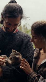 Embracing the joy of companionship, a couple shares laughter while cradling their cute kitten, surrounded by a tranquil misty backdrop that