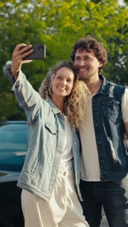 A happy couple enjoys a sunny day as they capture a playful selfie. Their smiles reflect the warmth and joy of their shared time outdoors in