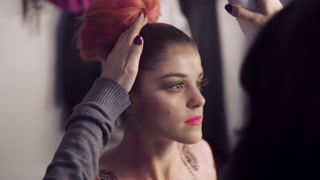 Hairstylist creates stunning hairdo for brunette model. Fashion show prep in dressing room.