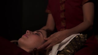 Massage therapist does thai massage of neck, head and face for woman on couch in spa room. Slow motion shot
