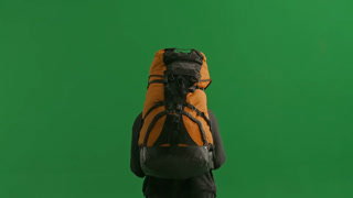 Back View of a Tired Hiker Walking with a Heavy Backpack on a Green Screen A Man Wipes Sweat From. Back view of a tired hiker walking with a heavy backpack on a green screen. A man wipes sweat from his forehead with his hand. Concept of outdoor adven