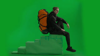 A Male Tourist with a Backpack on His Back Walks in the Studio on a Green Screen Close Up Side View. A male tourist with a backpack on his back walks in the studio on a green screen close up. Side view. Hiking trek rest travel trip concept