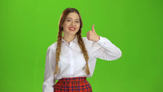 Young Woman Showing Smartphone with Green Screen Display. A smiling young woman holds a smartphone with a green screen, giving a thumbs up, set against a vibrant yellow backdrop.