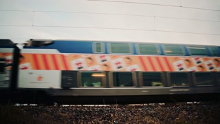 Side view of a high speed passenger train rushing along the tracks, decorated with bright promotional artwork