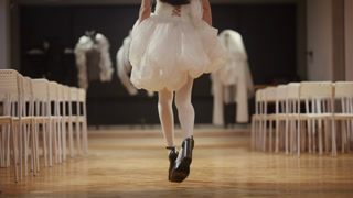 Close up of a model walking on a wooden runway floor, wearing a voluminous white dress with layered fabric and black high heels