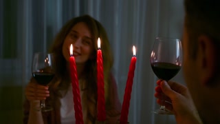 Mature lovely caucasian couple looking affectionate at each other and drink red wine on a romantic table with red candles. Evening date on Valentines day. Relationships and feelings concept. Rear view