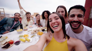 Excited young woman recording selfie video social media on rooftop. People gathered lunch.