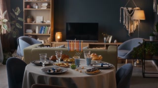 No people full shot of festive dinner table laid out for Hanukkah celebration including menorah with colored candles and plates with traditional foods in modern Jewish apartment