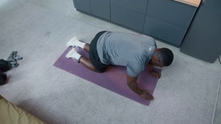 High angle slowmo of Black man in sportswear unrolling yoga mat on floor before training under house arrest on probation surveillance with electronic monitoring bracelet