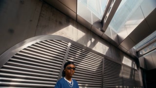 Stylish gen Z Black guy in y2k outfit standing in modern urban space near underground station entrance, looking at camera