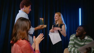 Diverse group of teenagers surprising Caucasian girl with birthday cake during acting rehearsal. Visual fits performing arts education, drama workshop campaigns, and youth community marketing