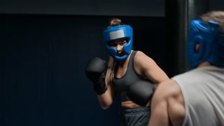 Male and female boxer in headgear and gloves facing off in controlled sparring session, demonstrating technique, timing, and mutual respect in professional gym setting