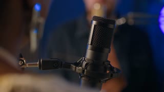 Cropped shot of podcasting process with unrecognizable blurred man and woman engaged in conversation speaking in professional microphone in focus