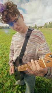 Vertical video of Caucasian young adult guitarist playing electric guitar in outdoor meadow. Clip suits indie music video production, musical gear advertising, social media promos