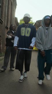 Three young Black guys wearing y2k streetstyle outfits vibing to hip-hop music while walking along side street