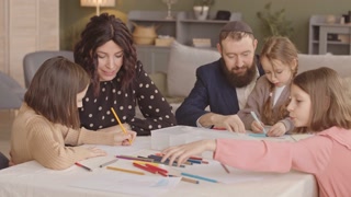 Delighted Jewish family of five sitting at table in living room together drawing postcards on Hanukkah