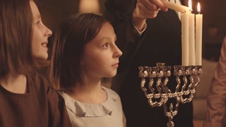 Children observing their father lighting menorah candles for Hanukkah at home