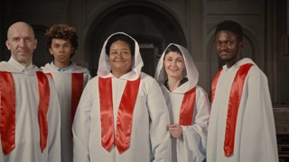 Zoom in portrait of multiethnic church choir in long white gowns smiling at camera standing in Catholic Church