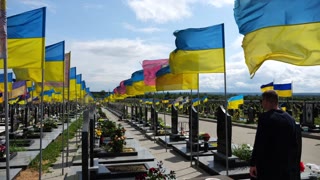 Mourning man walking among countless graves of Ukrainian soldiers with national flags at military cemetery in Kharkiv.