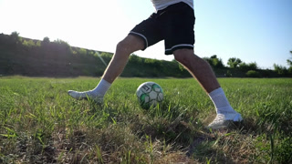 Male feet of professional footballer shows tricks with ball while running at green field. Legs of sportsman kicks ball during jogging at meadow on sunny day. Young man training at stadium. Slow motion