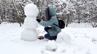 Happy woman building snowman at winter forest. Young girl having active leisure at snowy park. Cheerful female having fun outdoor. Concept