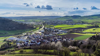 A town with roads, fields, pastures against the backdrop of silhouettes of hills and a cloudy sky