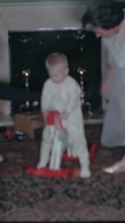 UNITED STATES - 1962 - A family watch a toddler walk and play on the carpet. The grandmother puts the child on the wooden rocking horse.