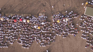 Seminyak, Indonesia - 21 March 2026: Aerial view of a gathering of people on the beach, some holding umbrellas, creating a pattern against the sand.