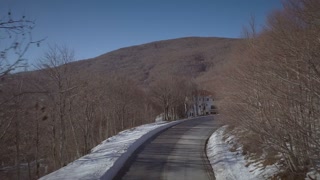 Aerial view of a snowy road with blue sky and a hill at the end.